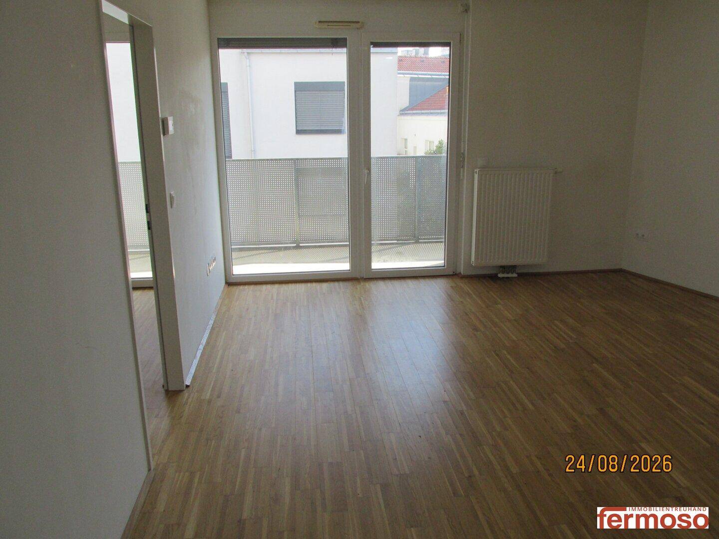 Geräumiges Wohnzimmer mit Holzboden und großen Schiebetüren zum Balkon, hell und einladend.