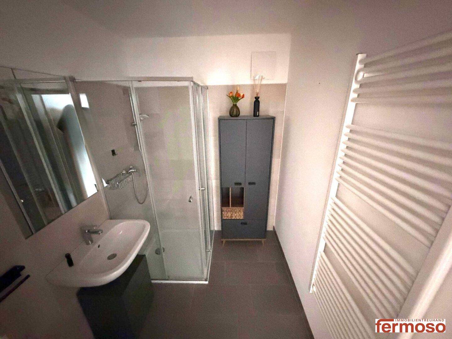 Funktionales Badezimmer mit Duschkabine, Einzelwaschbecken und beheiztem Handtuchhalter.