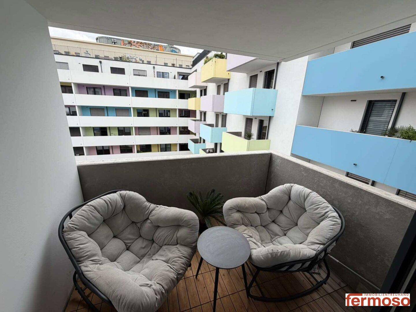 Gemütlicher Balkon mit Sitzgelegenheiten und Blick auf die farbenfrohe Fassade des Nachbargebäudes.