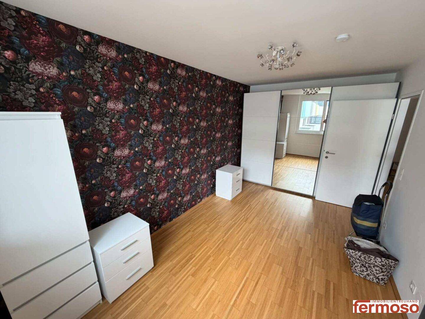 Geräumiges Schlafzimmer mit floraler Tapete, Holzboden und großem Spiegelschrank.