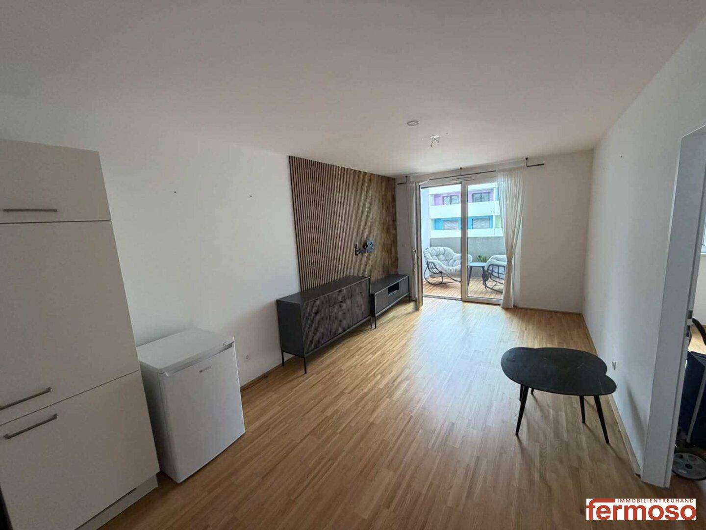 Heller Wohnbereich mit Holzboden, Medienmöbeln und direktem Zugang zum Balkon.