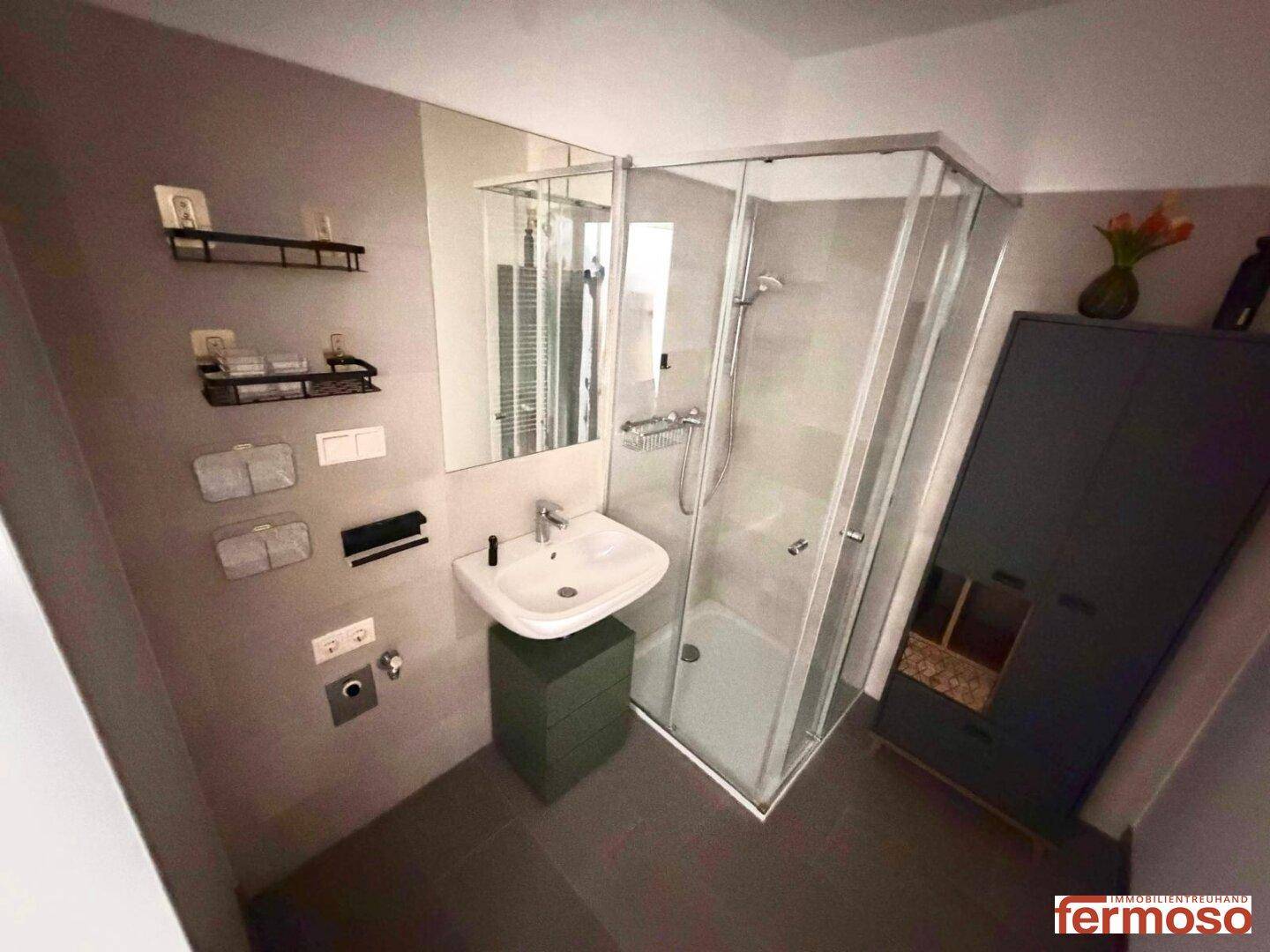 Modernes Badezimmer mit Duschkabine, Einzelwaschbecken und grauen Fliesen.