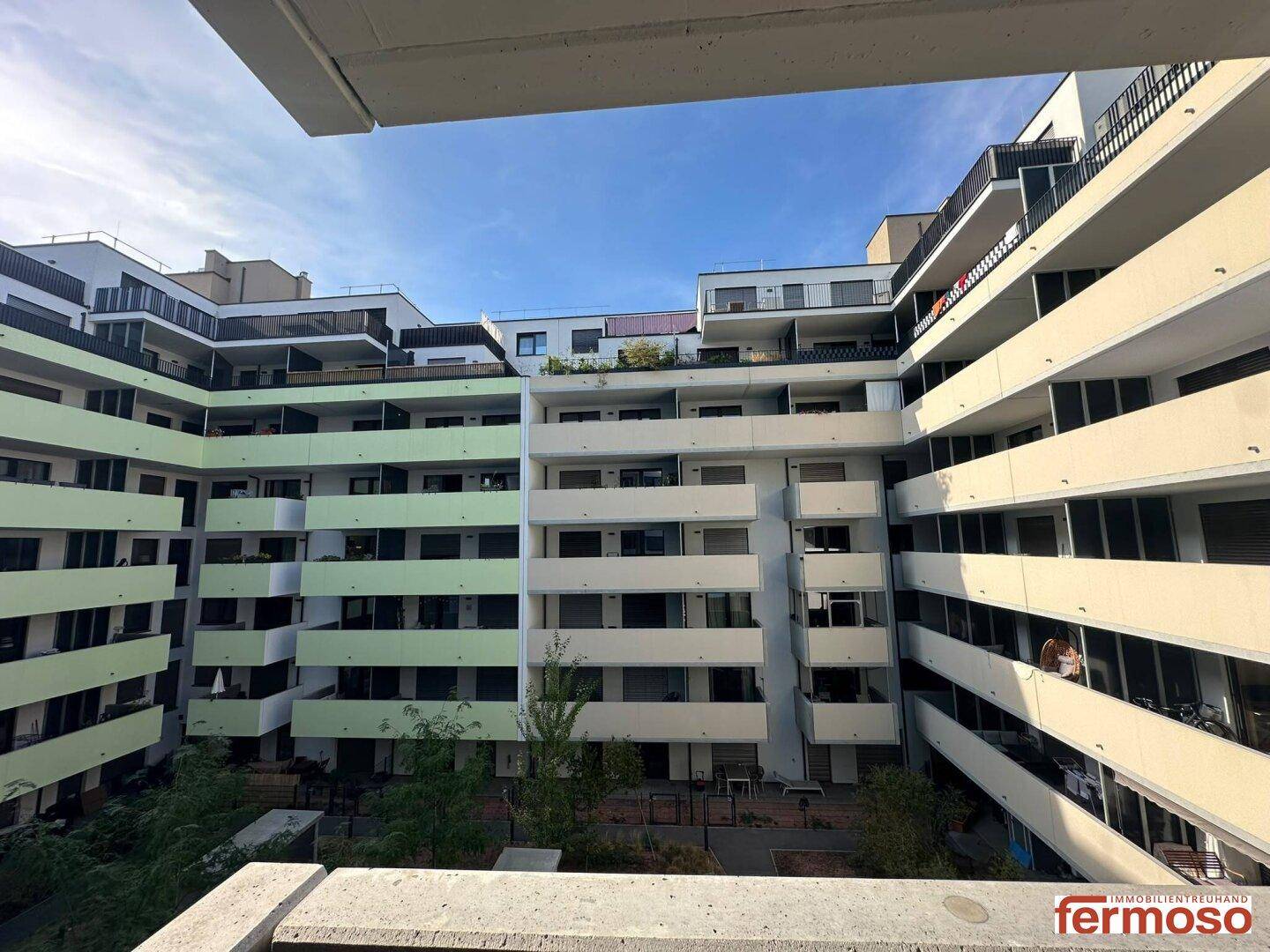 Blick vom Balkon auf den begrünten Innenhof einer modernen Wohnanlage mit vielen Balkonen.