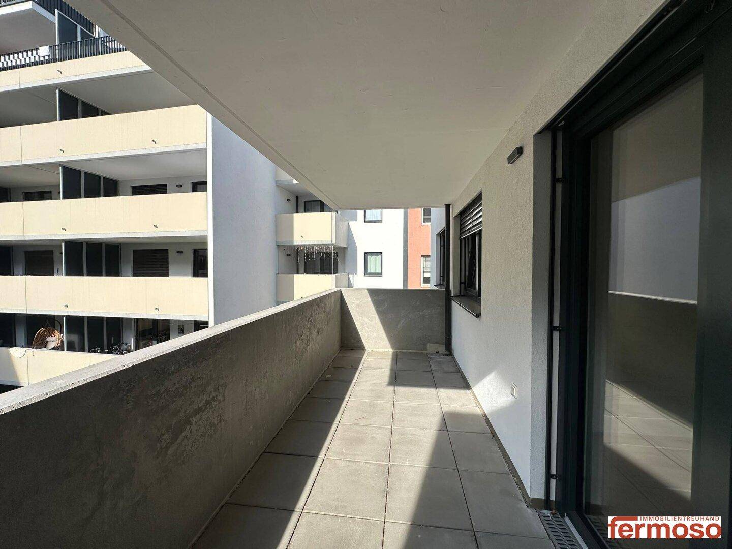 Langer Balkon mit Fliesenboden und seitlichem Blick auf die moderne Gebäudefassade.