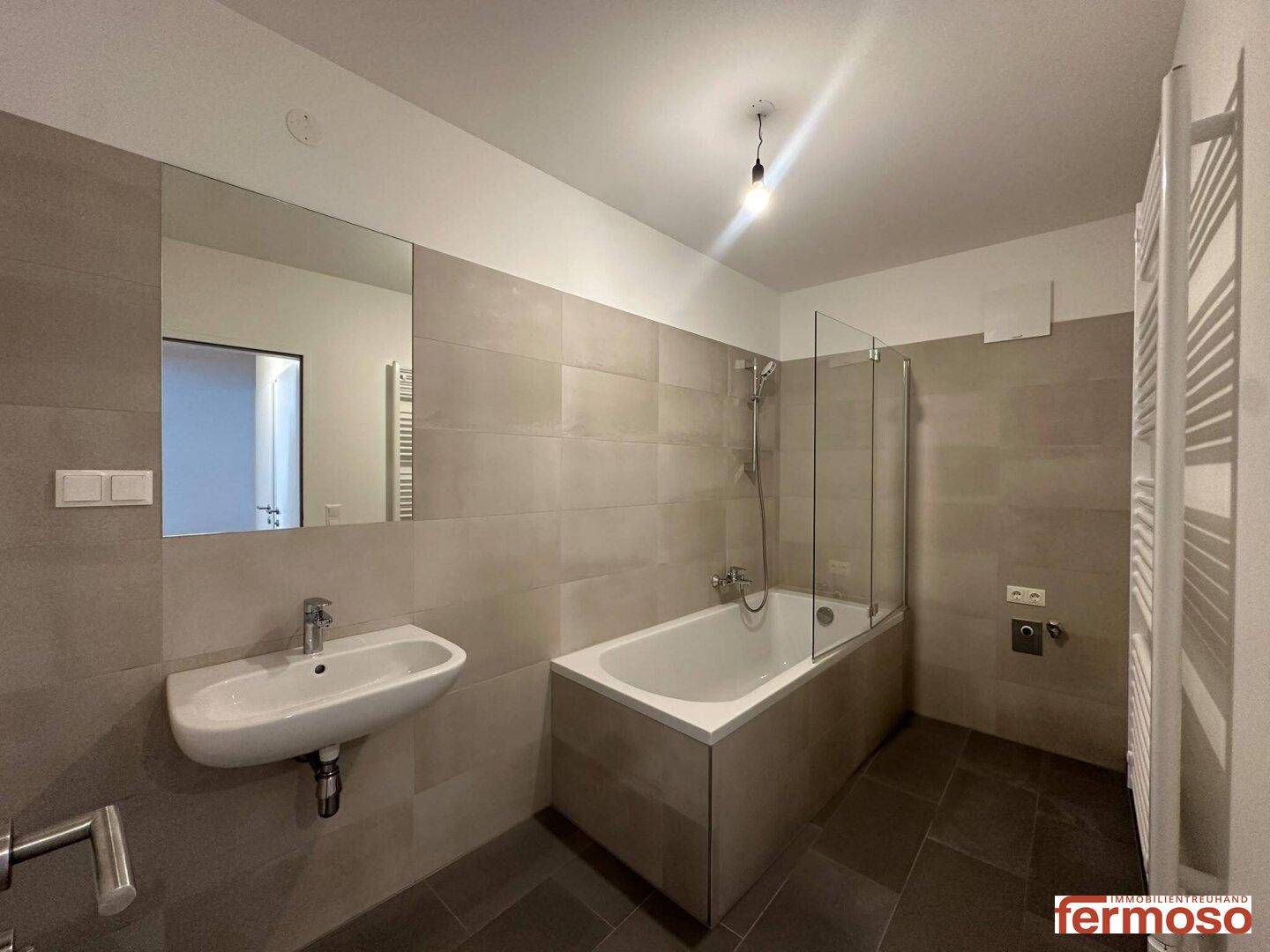 Modernes Badezimmer mit Badewanne, Duschwand, Waschbecken und beheiztem Handtuchhalter.