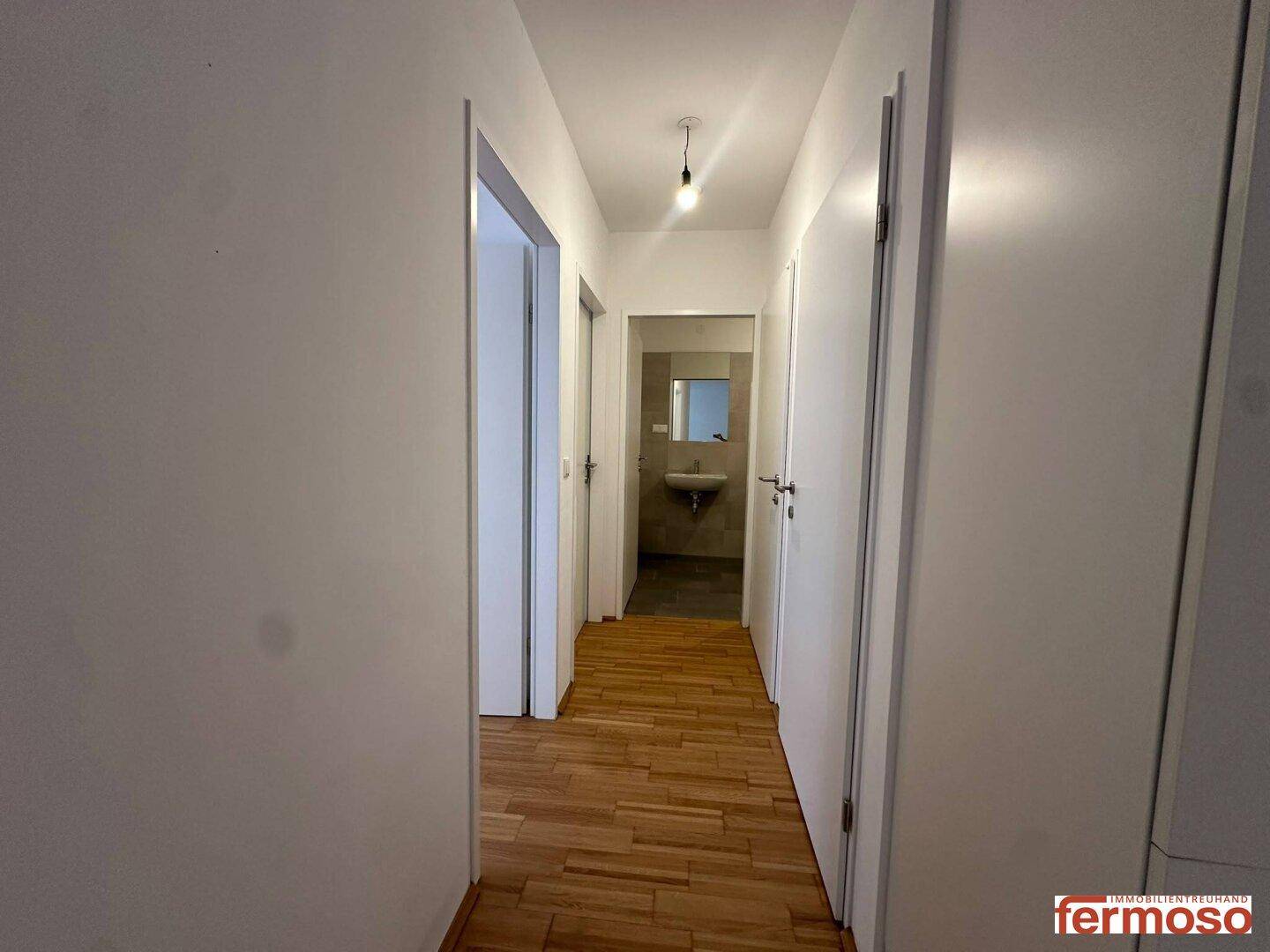 Heller Flur mit Parkettboden und Zugang zu verschiedenen Räumen, inklusive Badezimmer.