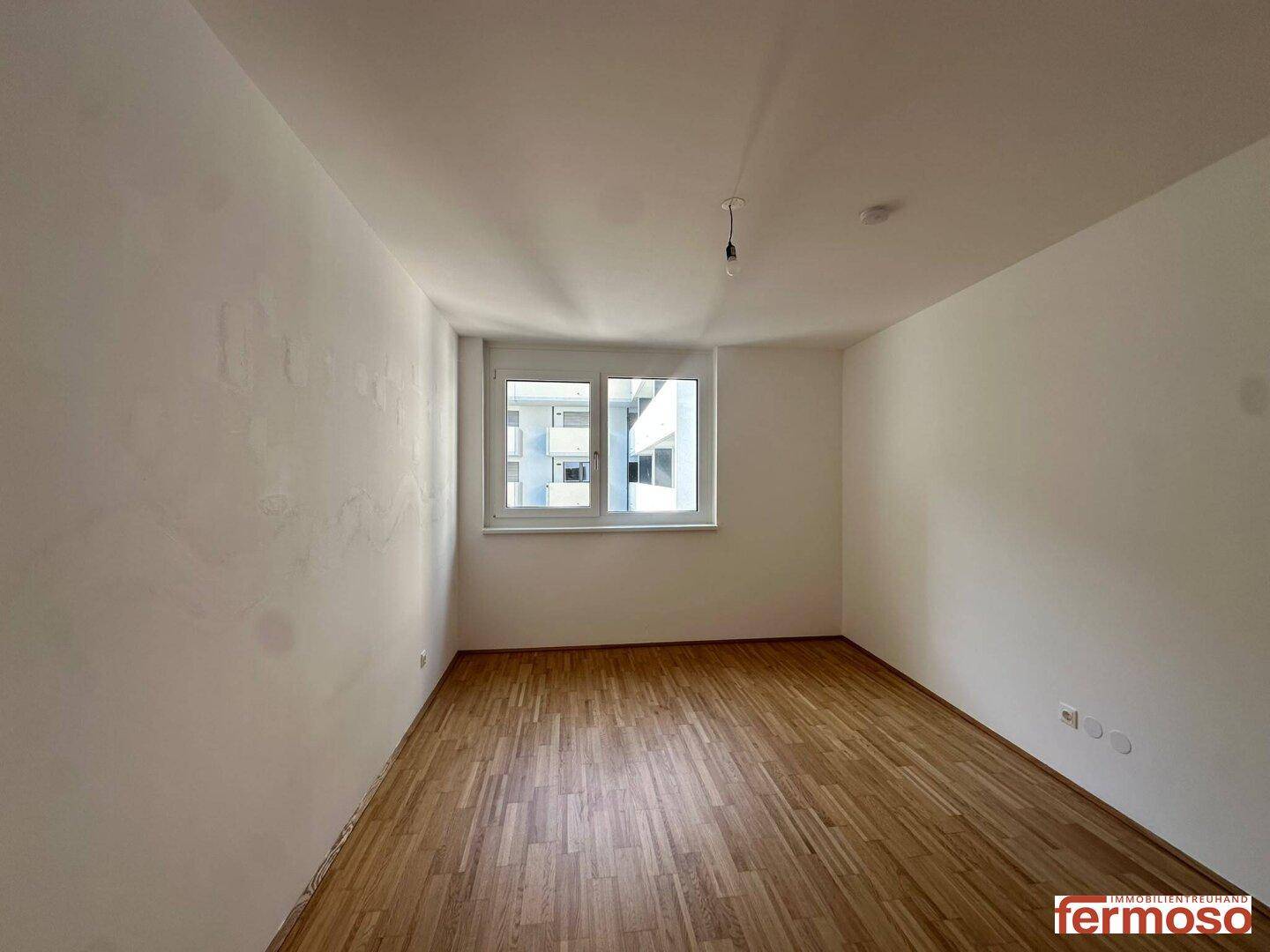 Leeres Zimmer mit Parkettboden und großem Fenster, ideal als Schlaf- oder Arbeitszimmer.