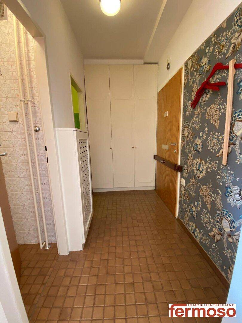 Flur mit Fliesenboden, Einbauschränken und dekorativer Tapete an einer Wand.