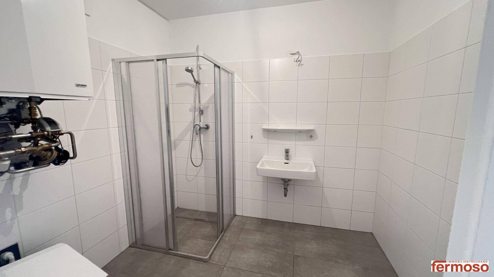 Funktionales Badezimmer mit Duschkabine, Waschbecken und weißen Fliesen an den Wänden.