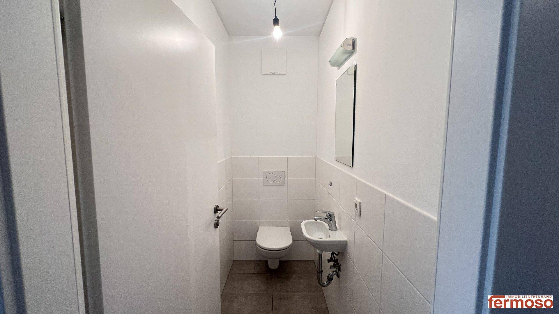 Kleines Gäste-WC mit Toilette, Waschbecken und Spiegel, ausgestattet mit weißen Fliesen.