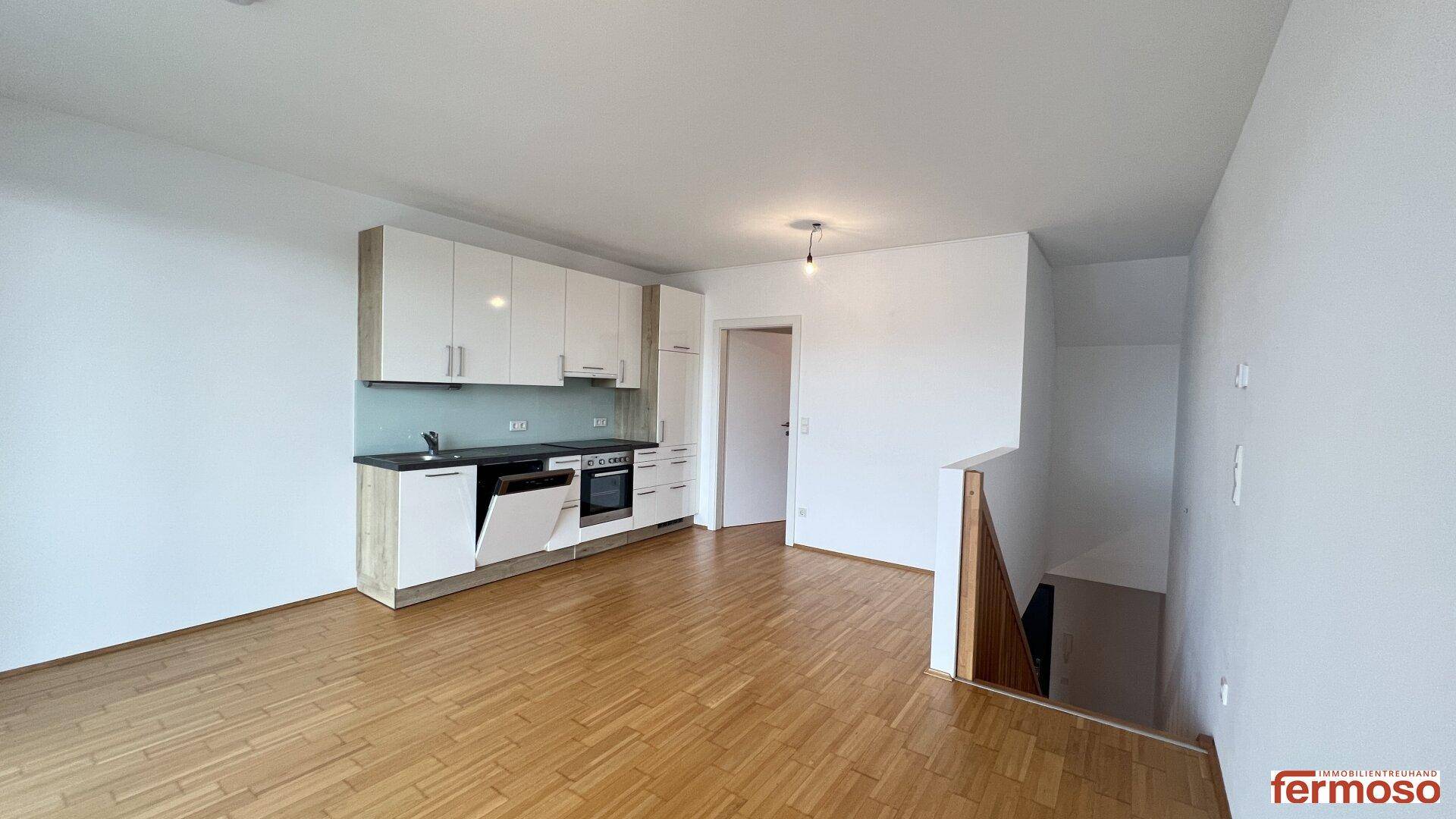 Offener Wohnbereich mit integrierter Einbauküche und Treppenzugang zu einer weiteren Etage.