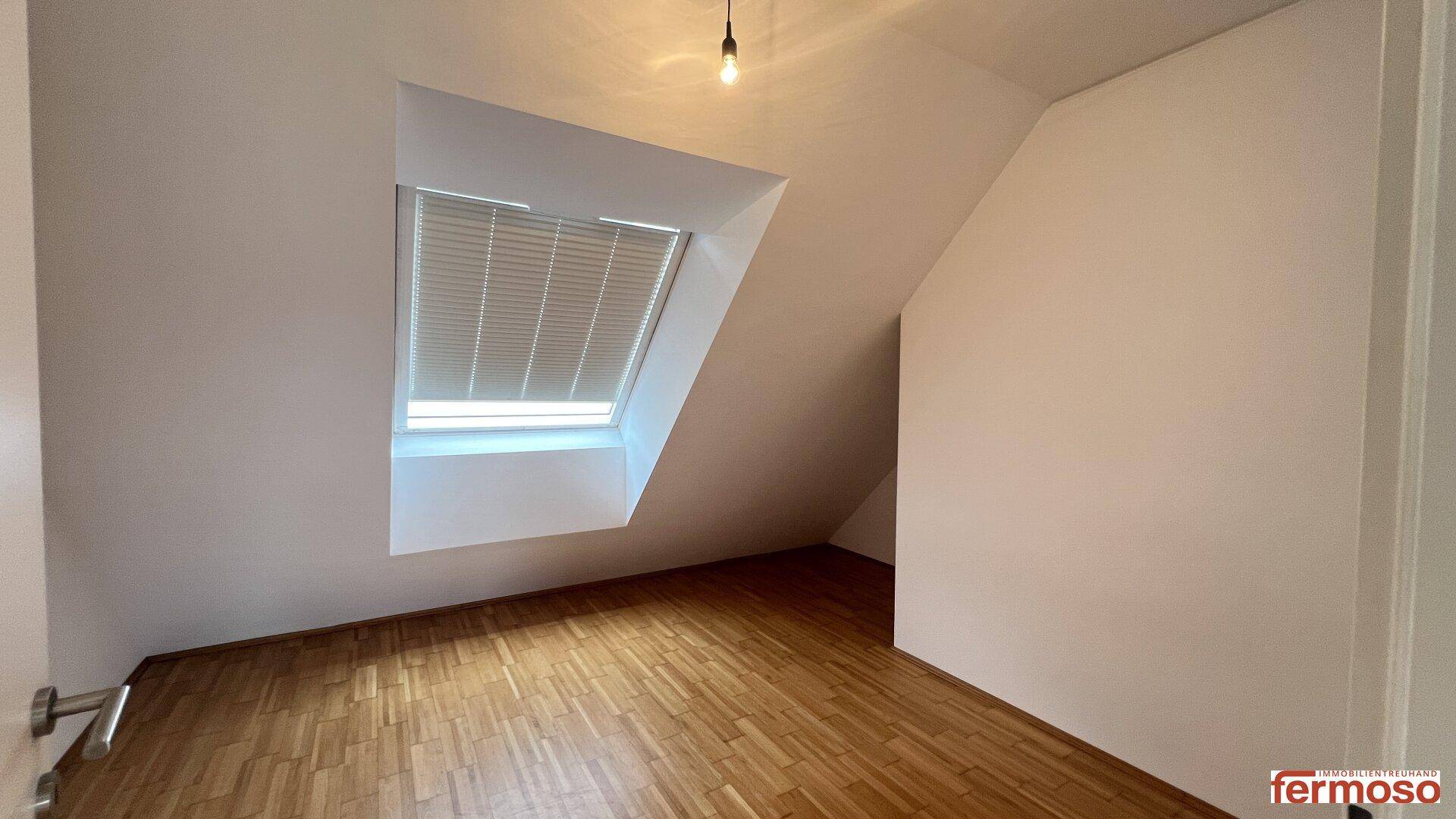 Helles Schlafzimmer im Dachgeschoss mit Holzboden, Dachschräge und einem großen Dachfenster.