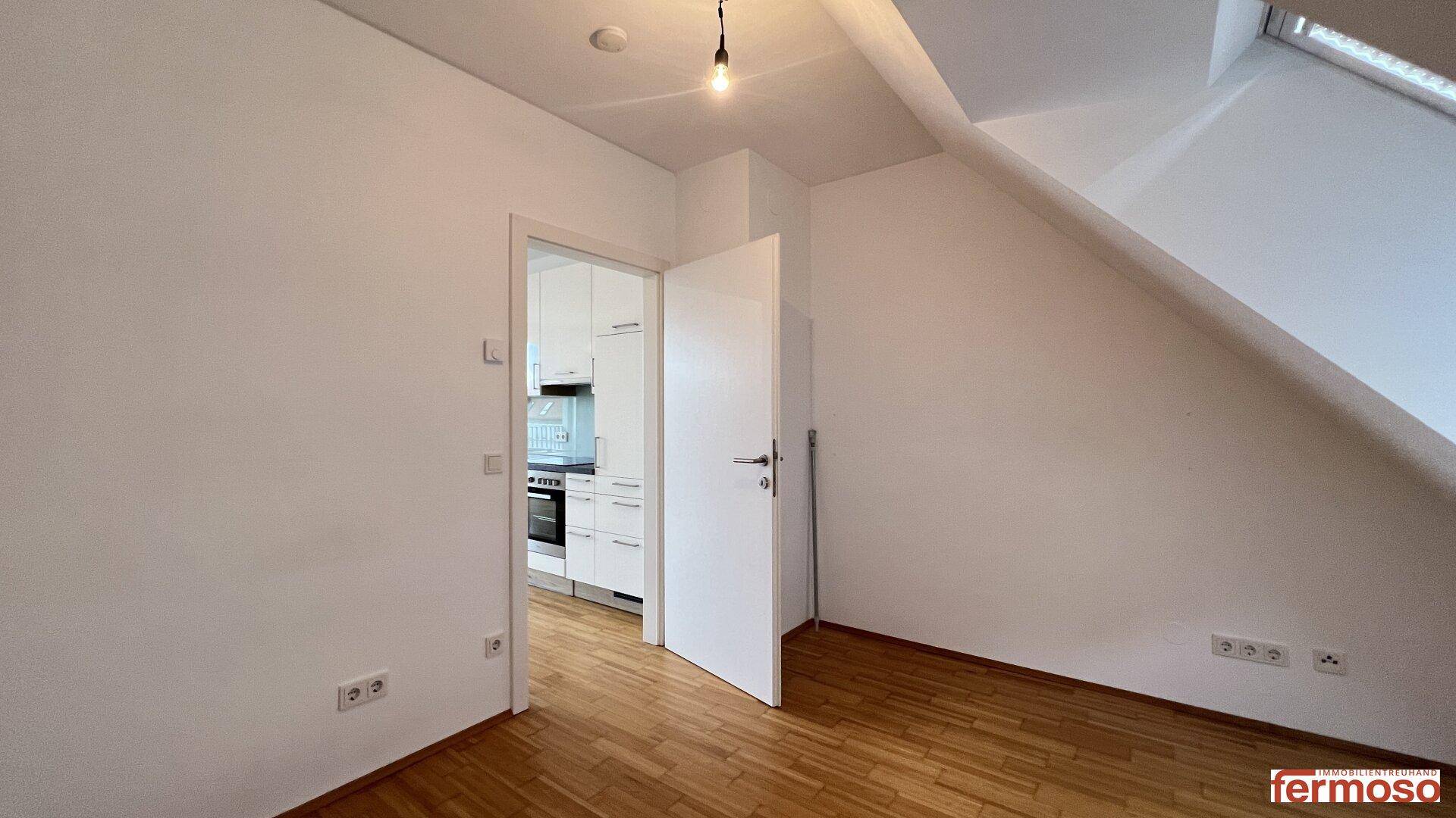 Leerer Raum mit Holzboden und weiß gestrichenen Wänden, mit Zugang zu einem weiteren Zimmer.