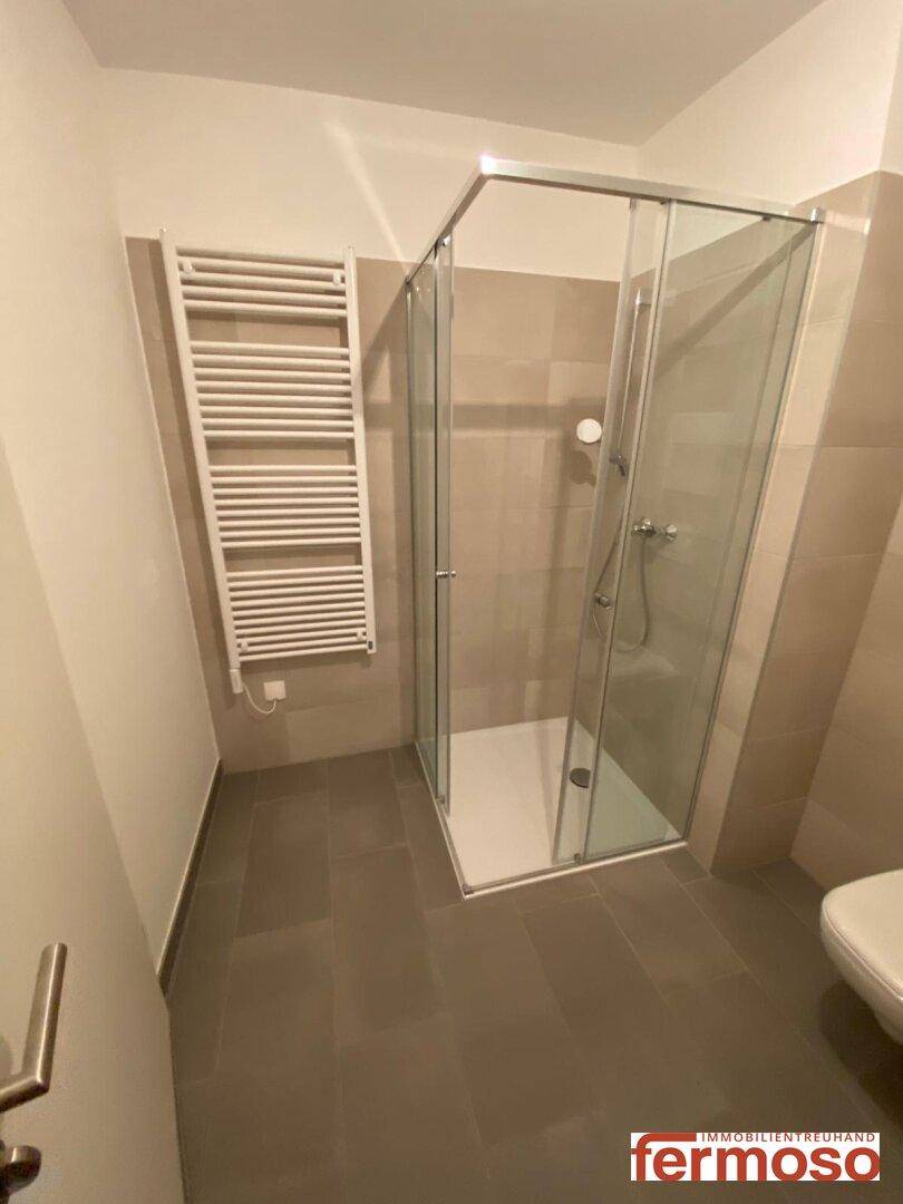 Modernes Badezimmer mit Duschkabine, beheiztem Handtuchhalter und hellen Fliesen.