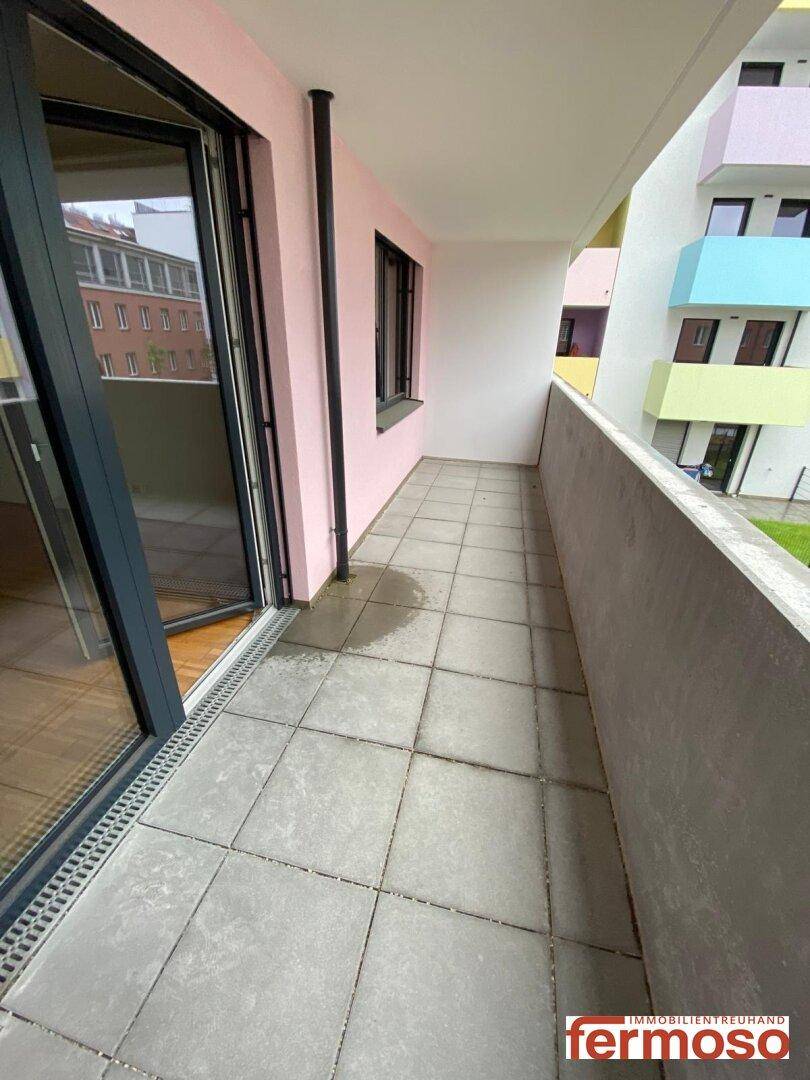 Langer Balkon mit grauen Fliesen und Blick auf die umliegenden Gebäude.