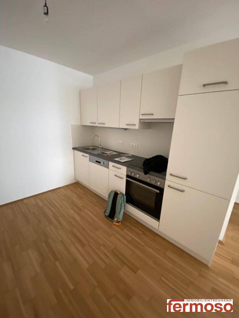 Funktionale Einbauküche mit weißen Schränken, Spülmaschine und Herd auf Holzparkettboden.
