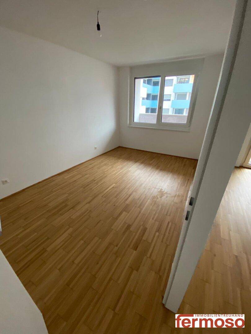 Helles Zimmer mit Holzparkettboden und großem Fenster, bietet Blick auf die Umgebung.