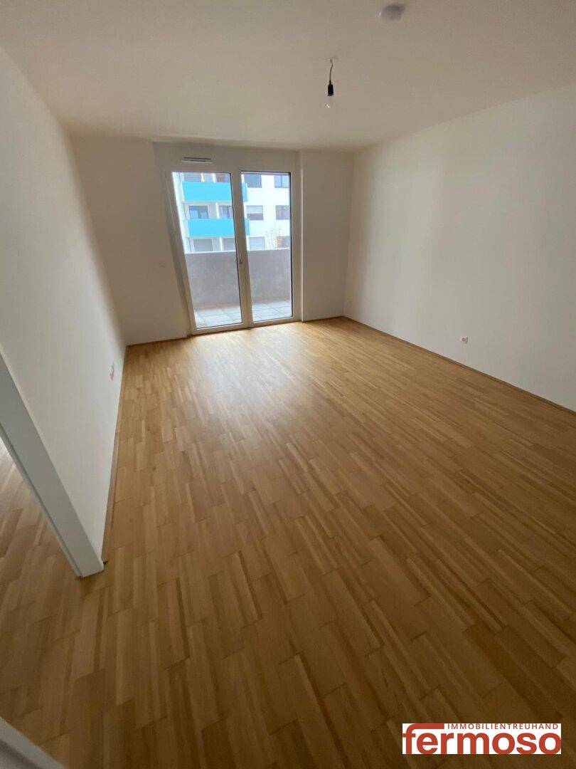 Geräumiges Zimmer mit Holzparkettboden und Zugang zum Balkon durch eine große Glastür.