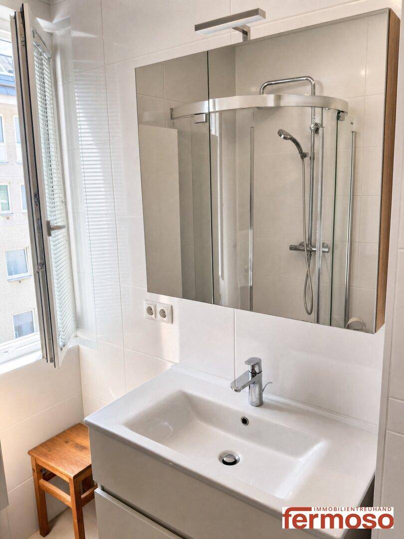 Modernes Badezimmer mit Waschtisch, Spiegelschrank, Duschkabine und Fenster für Tageslicht.