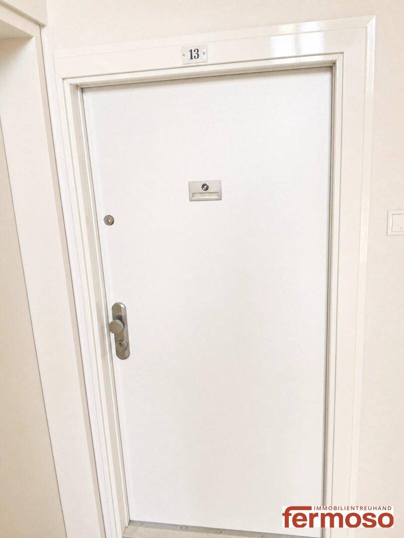 Weiße Wohnungseingangstür mit Nummer 13 in einem hellen Flur des Gebäudes.