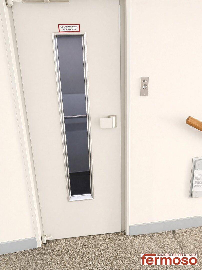 Heller Flurbereich mit moderner Aufzugstür und Bedienelementen im Mehrfamilienhaus.