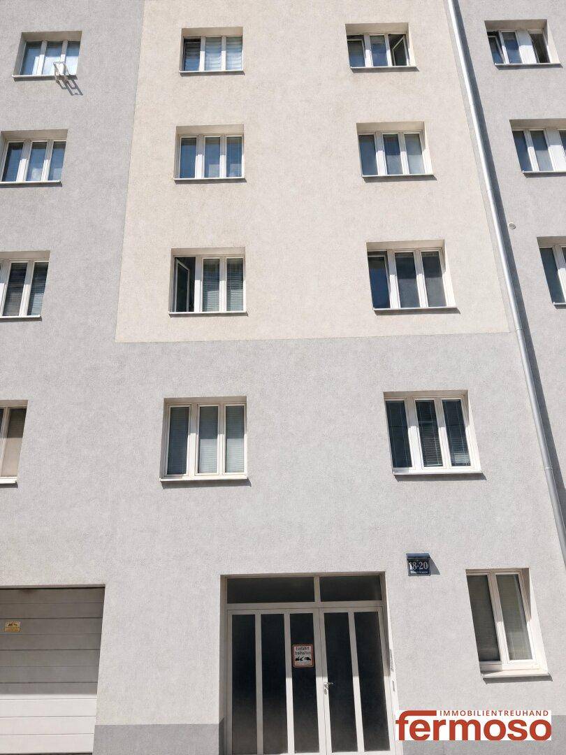 Moderne Wohnhausfassade in hellen Grautönen mit zahlreichen Fenstern und Eingangsbereich.
