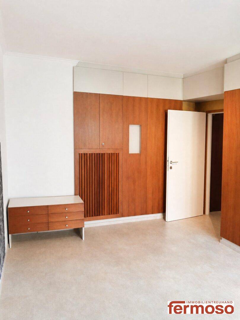 Leeres Schlafzimmer mit integrierten Holzschränken und hellem Fliesenboden, bereit zur individuellen Gestaltung.