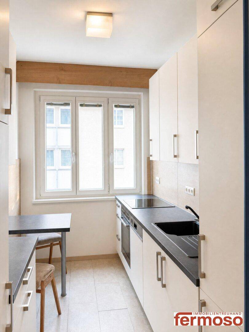 Funktionale Küche mit weißen Schränken, dunkler Arbeitsplatte und Fenster für natürliches Licht.