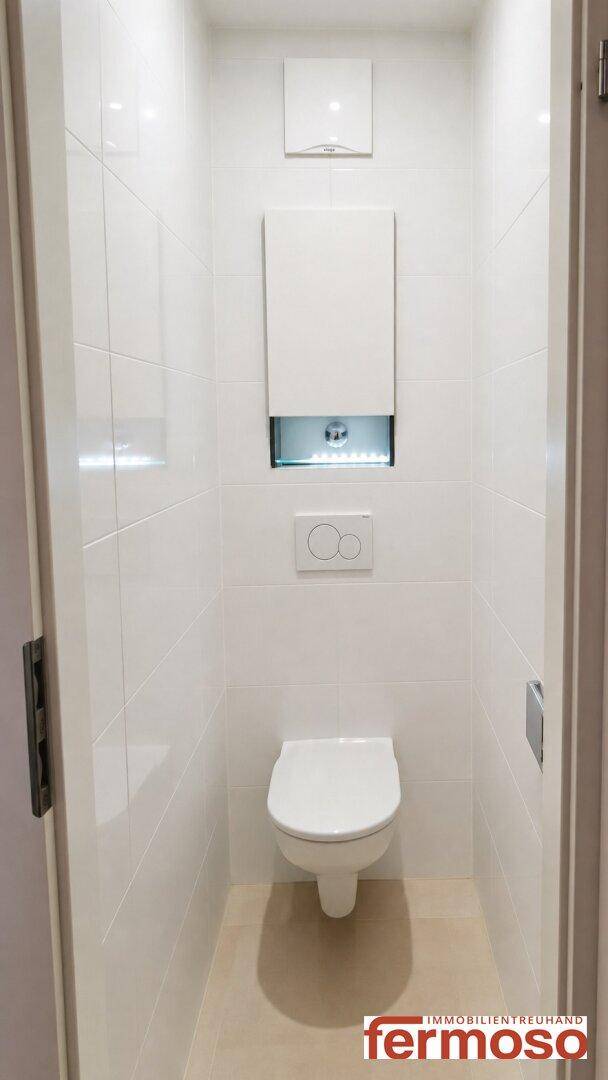 Separates WC mit wandhängender Toilette und weißen Fliesen, minimalistisch und sauber.