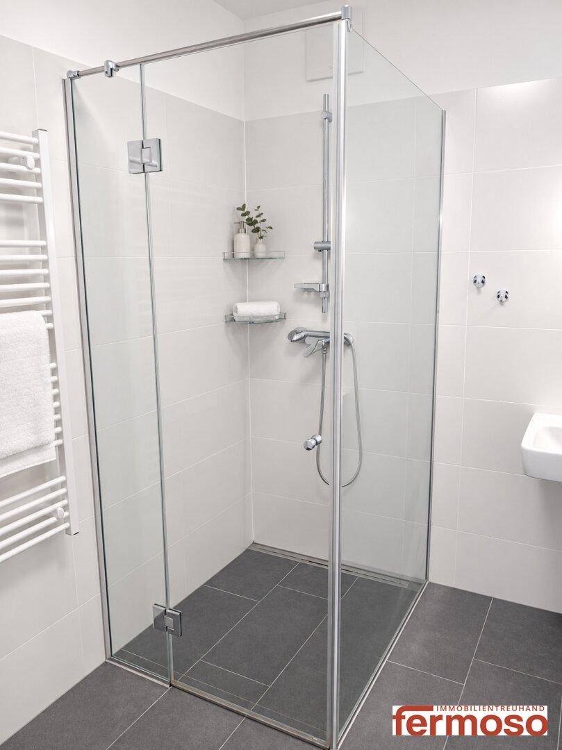 Modernes Badezimmer mit Glasdusche, Handtuchheizkörper und hellen Fliesen.