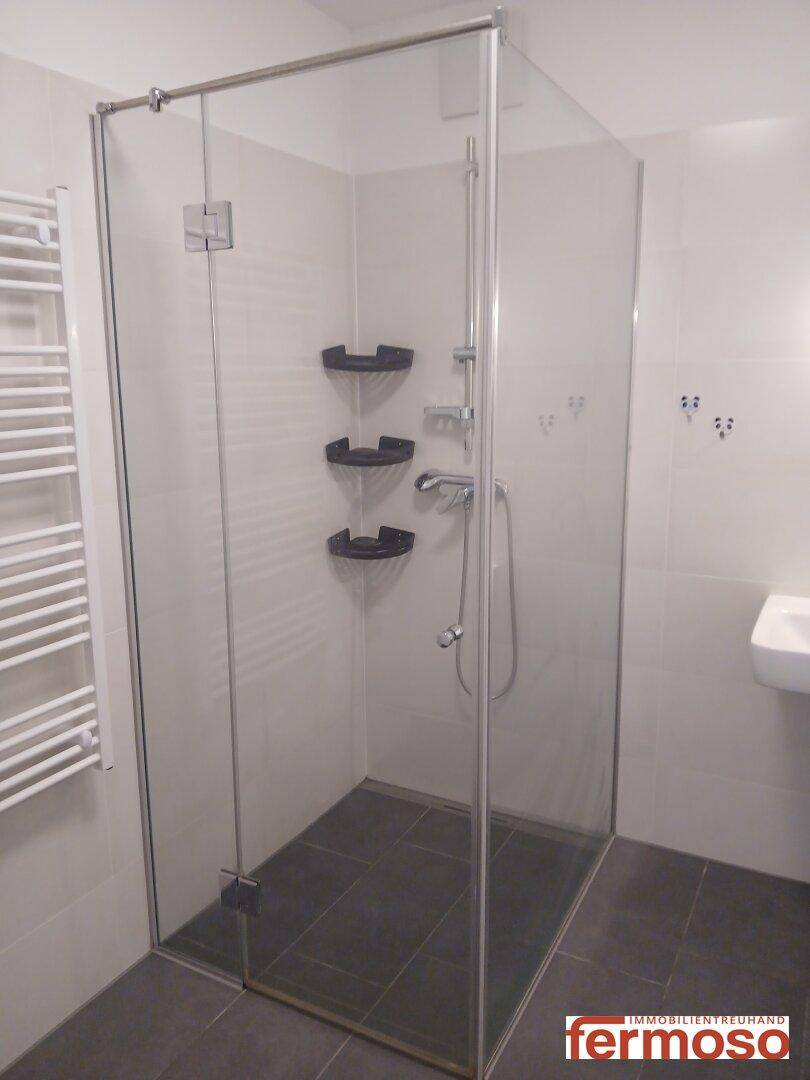 Leeres Badezimmer mit Glasdusche, Handtuchheizkörper und hellen Fliesen.