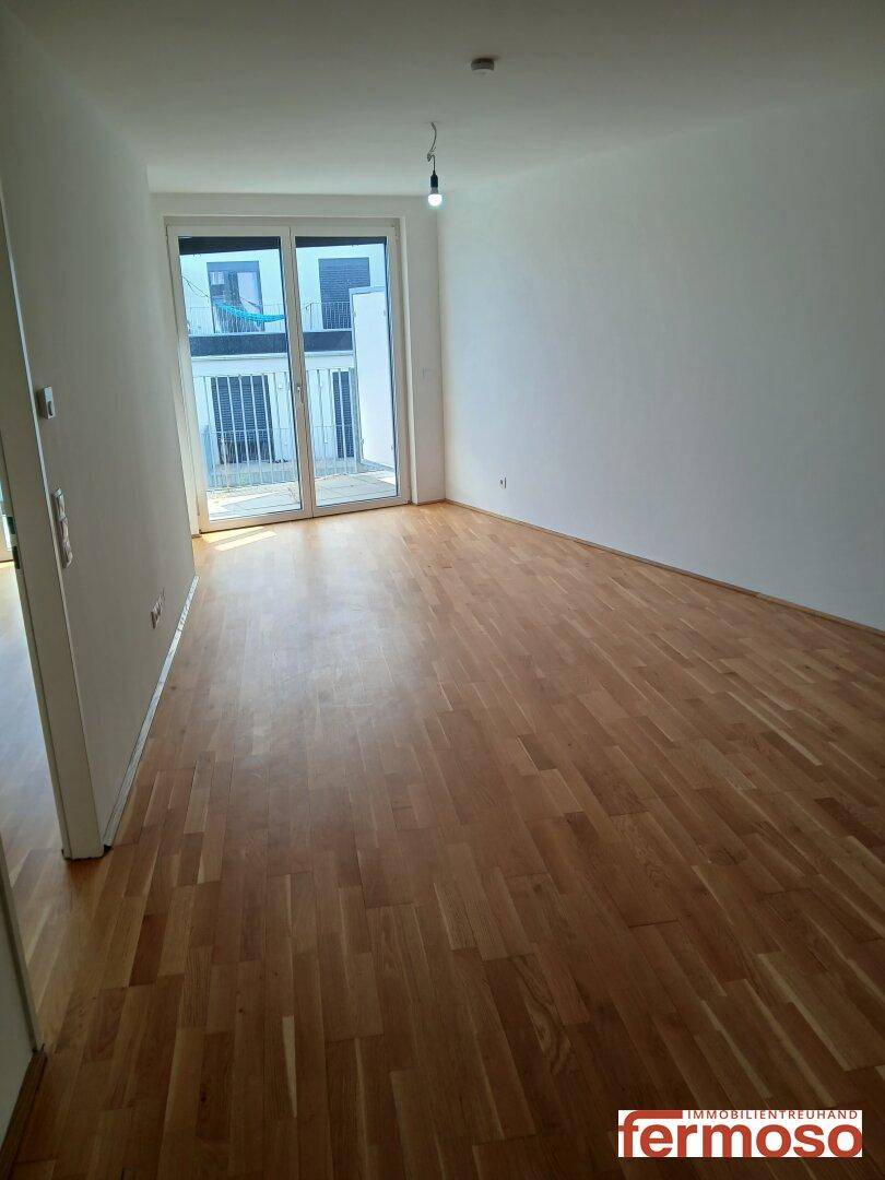Leeres Wohnzimmer mit Parkettboden und Zugang zum Balkon, hell und geräumig.