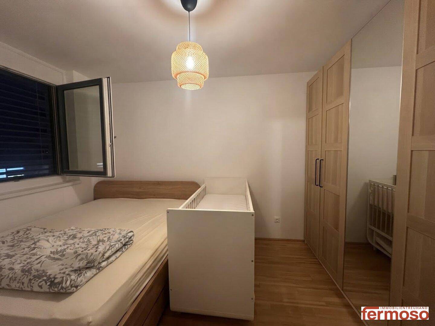 Schlafzimmer mit Doppelbett, Babybett und großem Spiegelschrank, hell und funktional eingerichtet.