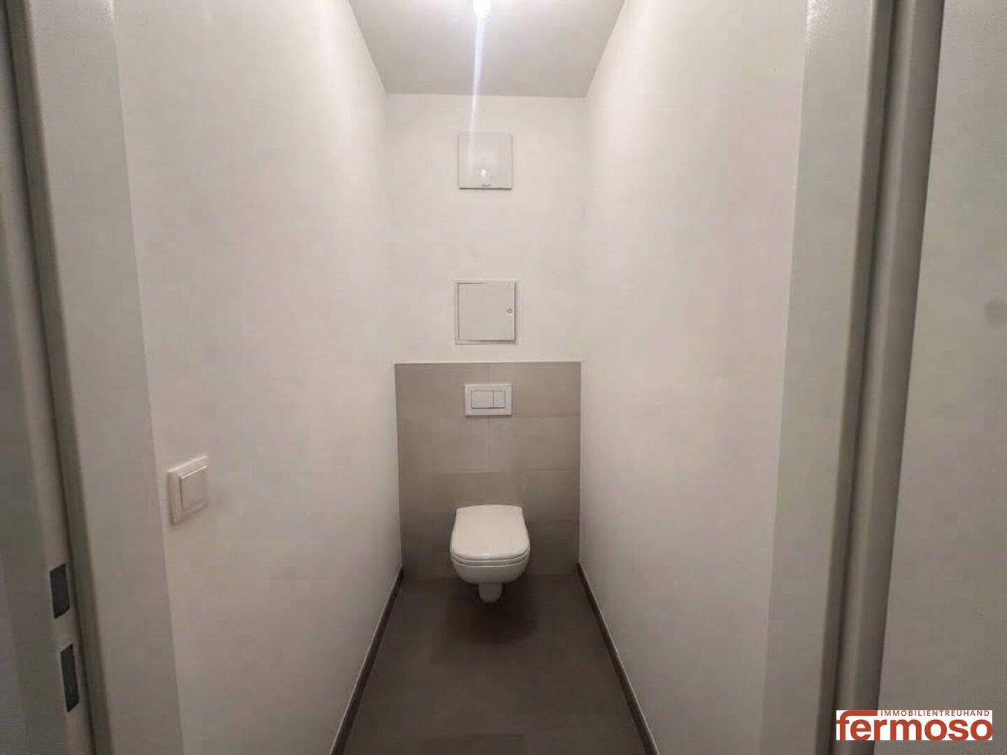 Separates Gäste-WC mit wandhängender Toilette und grauen Fliesen im unteren Bereich.
