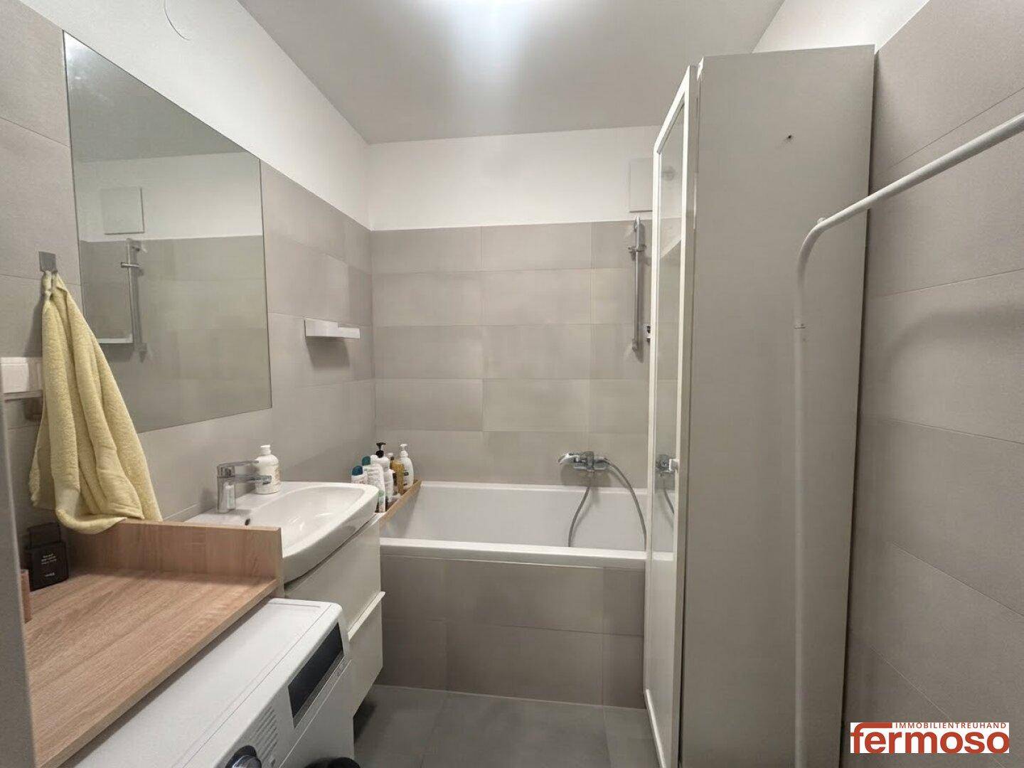 Modernes Badezimmer mit Badewanne, Waschbecken und großem Spiegel, hell gefliest.