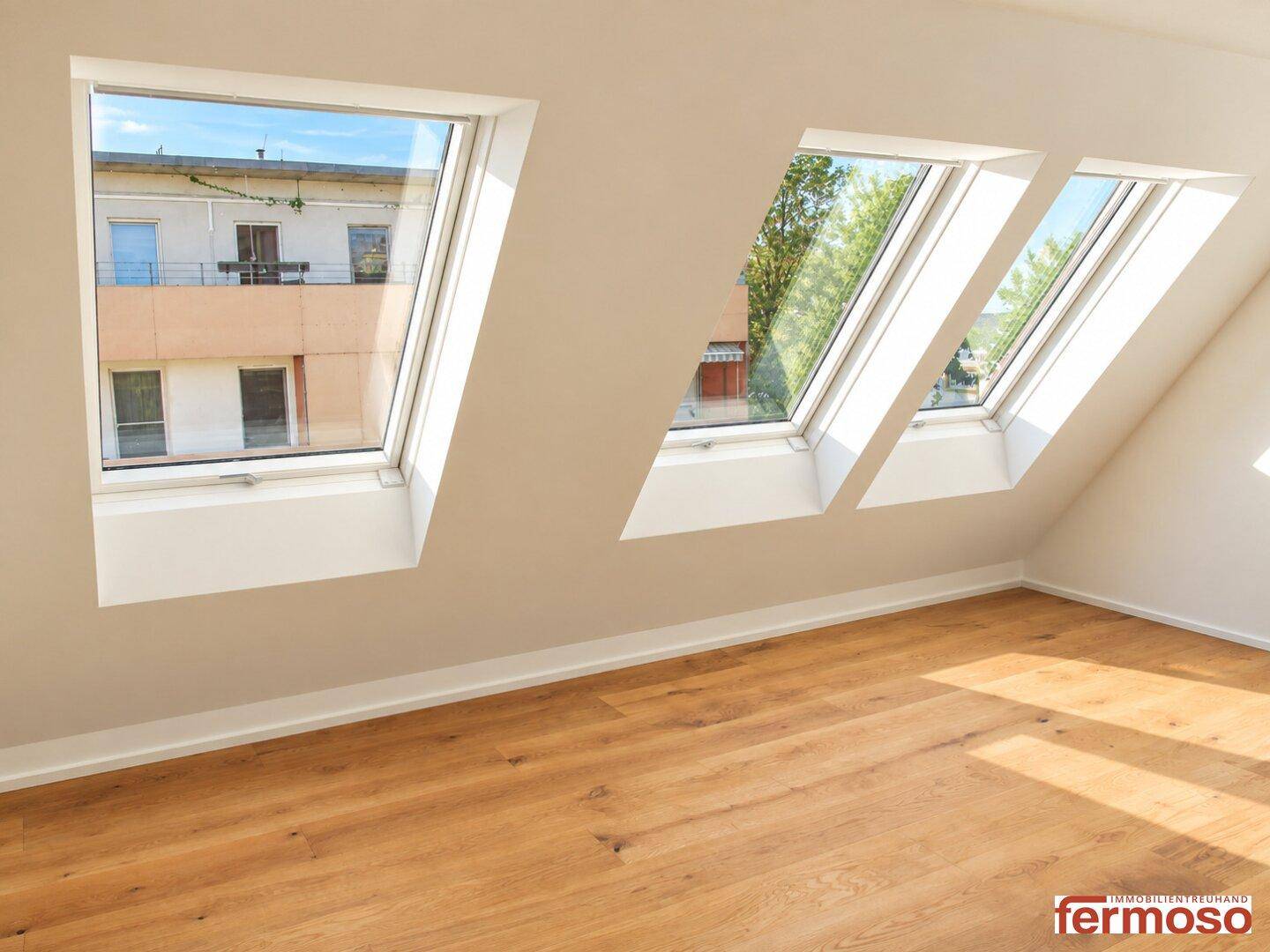 Heller Dachgeschossraum mit Holzboden und drei großen Dachfenstern, die viel Tageslicht hereinlassen.