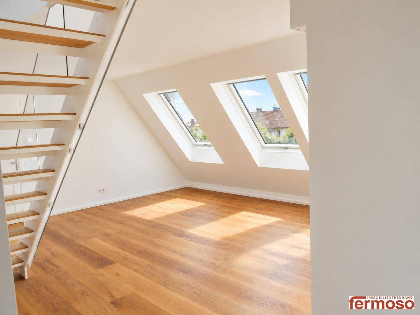 Geräumiger Dachgeschossraum mit moderner Holztreppe und großen Dachfenstern, die den Raum erhellen.