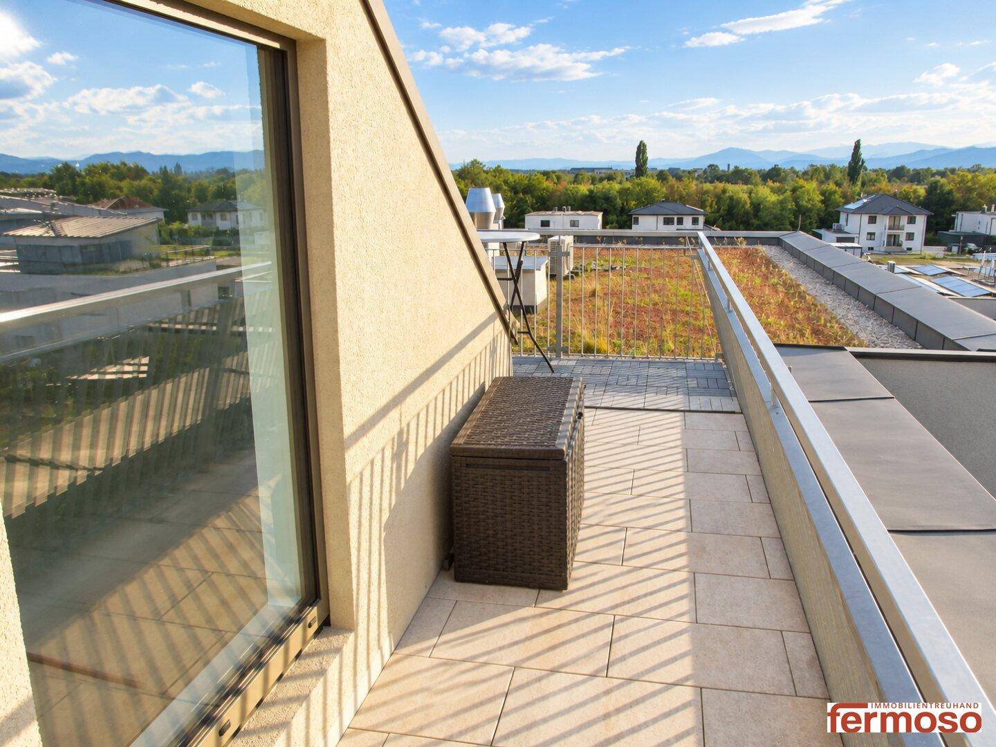 Kleine Terrasse mit Blick auf die grüne Dachfläche und die umliegende Berglandschaft in der Ferne.