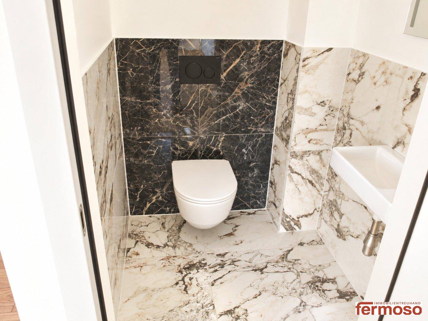 Elegantes Gäste-WC mit wandhängender Toilette und Marmorfliesen an Wänden und Boden.