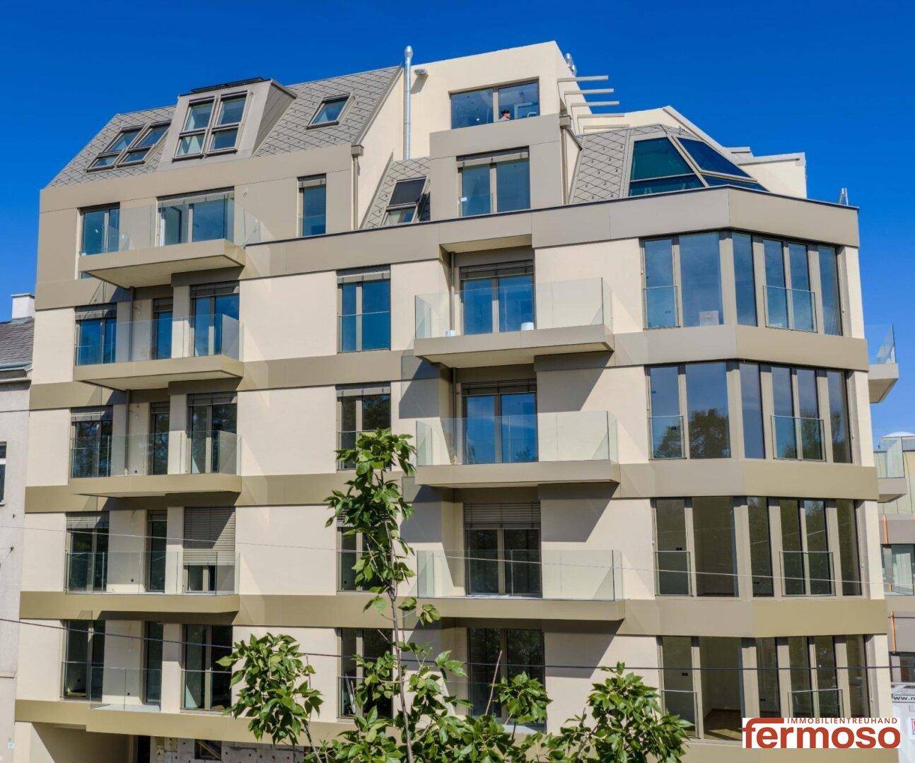 Moderne Wohngebäude-Fassade mit mehreren Balkonen und großen Fenstern unter blauem Himmel.