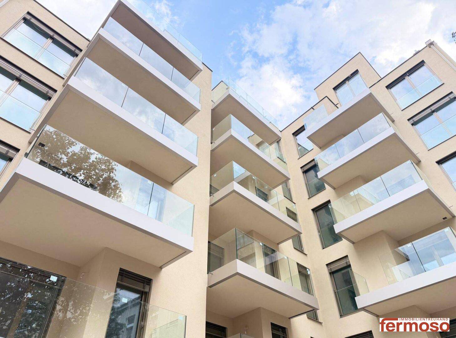 Moderne Gebäudefassade mit vielen Balkonen und Glasgeländern unter blauem Himmel.