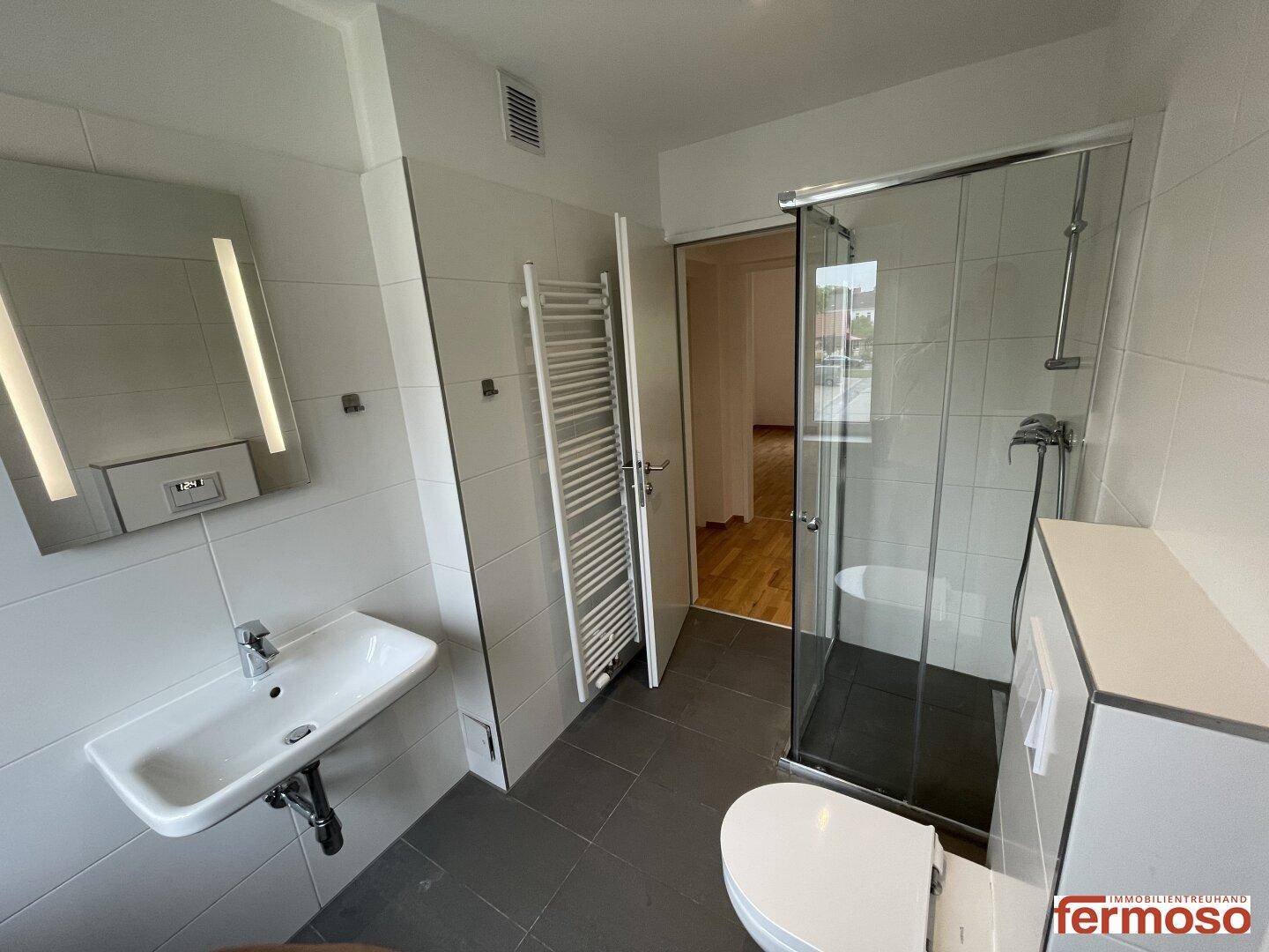 Modernes Badezimmer mit Duschkabine, Wand-WC, Waschbecken und beheiztem Handtuchhalter.
