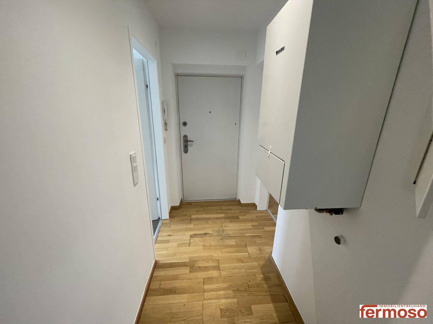 Eingangsbereich mit heller Holzboden und einer modernen Gegensprechanlage an der Wand.