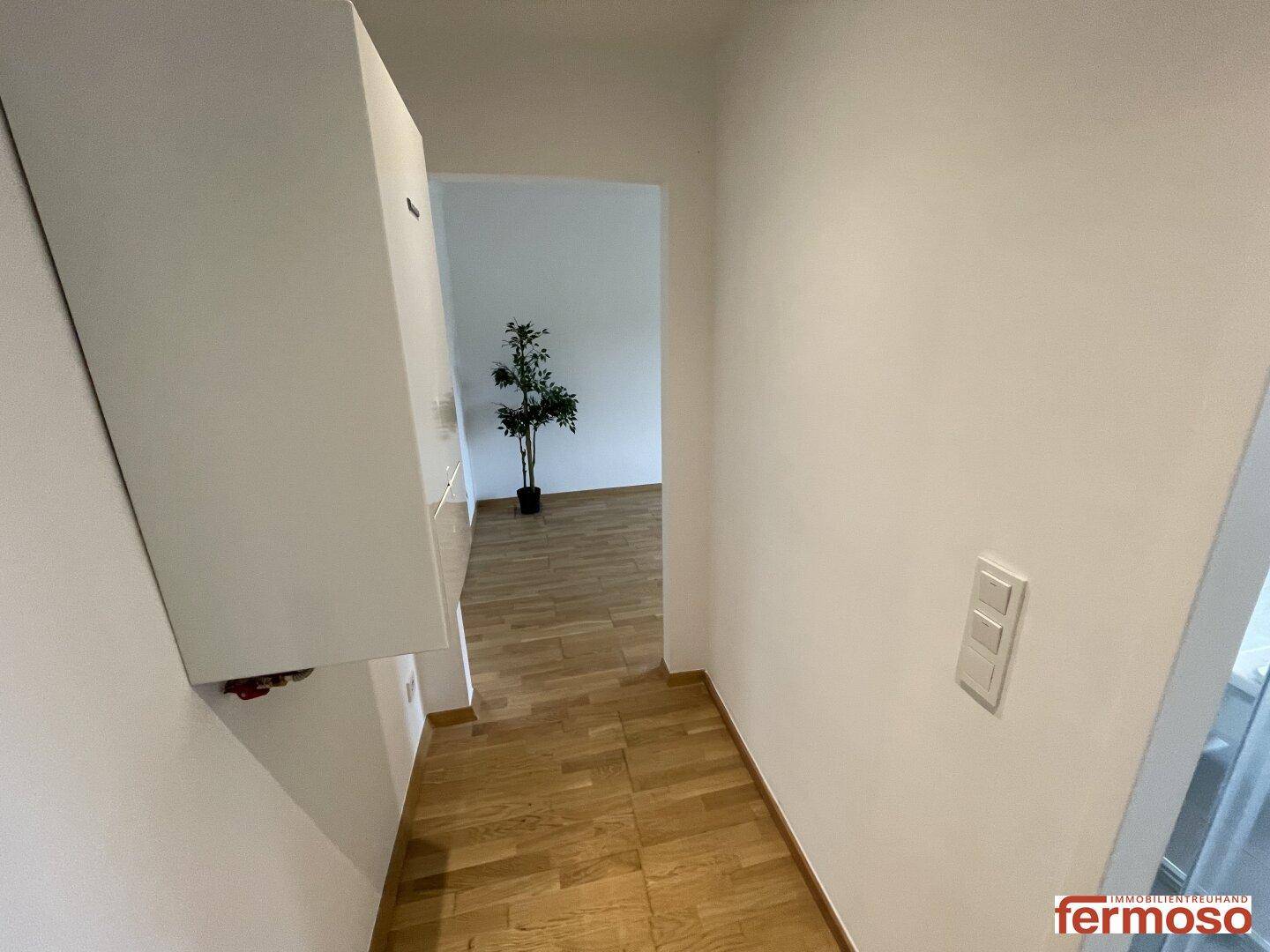 Heller Flur mit Parkettboden und Zugang zu weiteren Räumen, ausgestattet mit einem Wandregal.