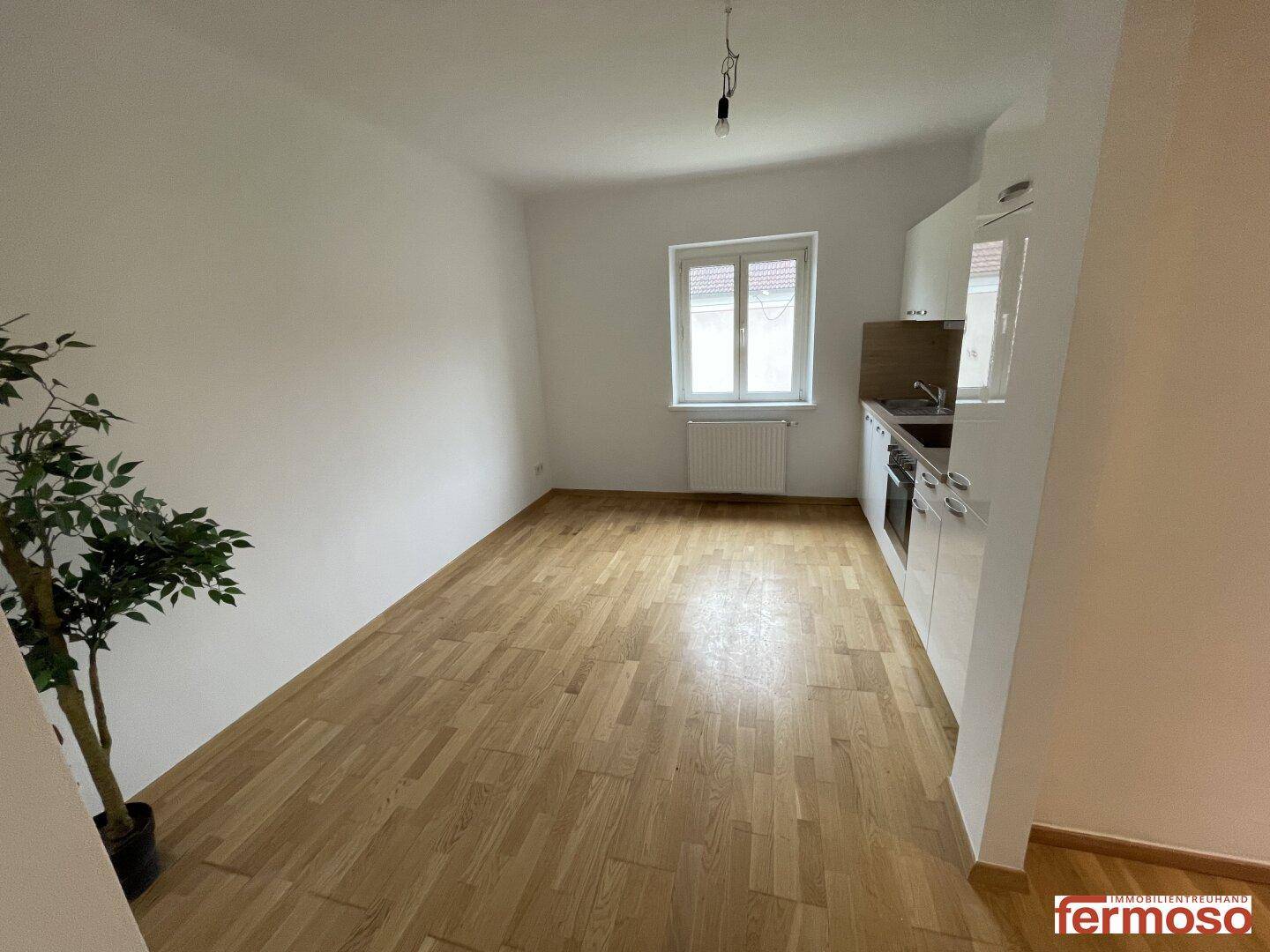 Heller Wohnbereich mit Parkettboden und einem Fenster, das viel Tageslicht hereinlässt.