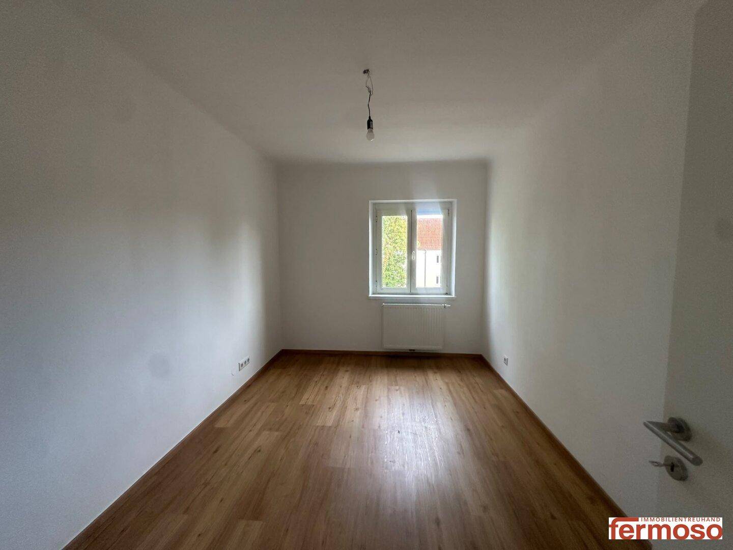Leeres Zimmer mit hellem Laminatboden und weiß gestrichenen Wänden, ideal als Schlafzimmer.