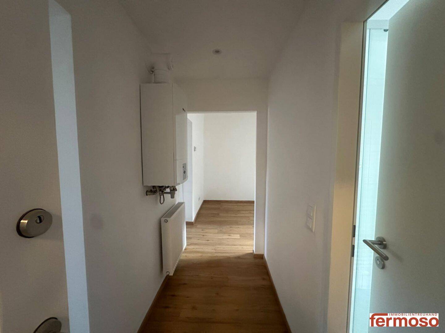Heller Flur mit Laminatboden und Heizungsanlage, der zu weiteren Räumen führt.