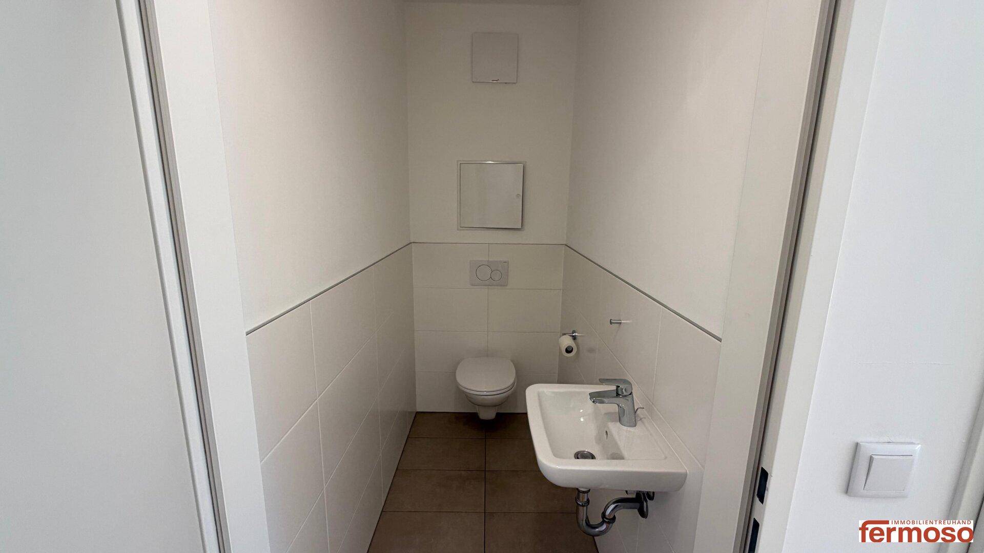 Kleines Gäste-WC mit Toilette, Waschbecken und weißen Fliesen an den Wänden.