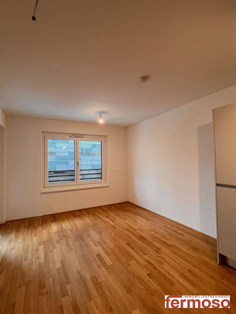 Geräumiges Wohnzimmer mit hellem Parkettboden und großem Fenster.