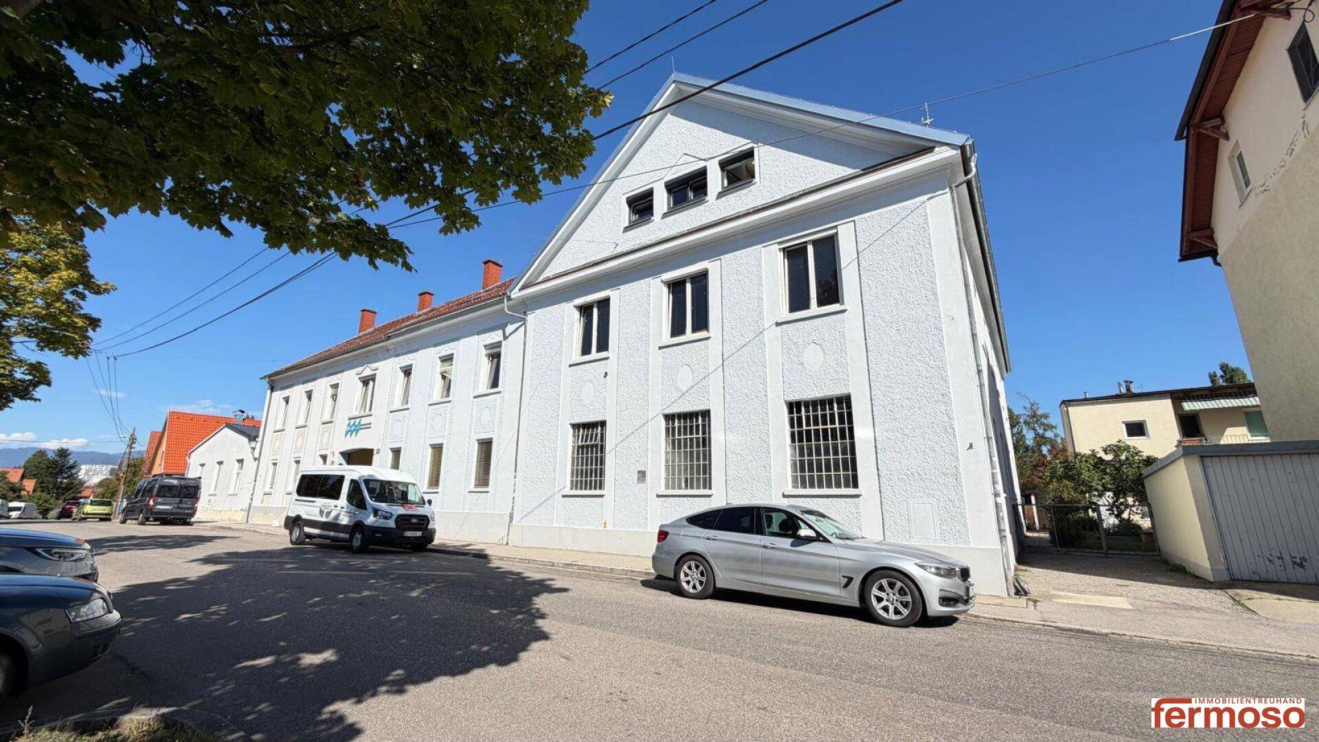 Weißes Mehrfamilienhaus mit schlichter Fassade und parkenden Autos an der Straße.